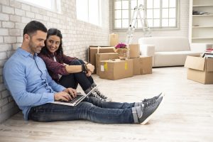 couple sitting on floor using a laptops with moving boxes in backround