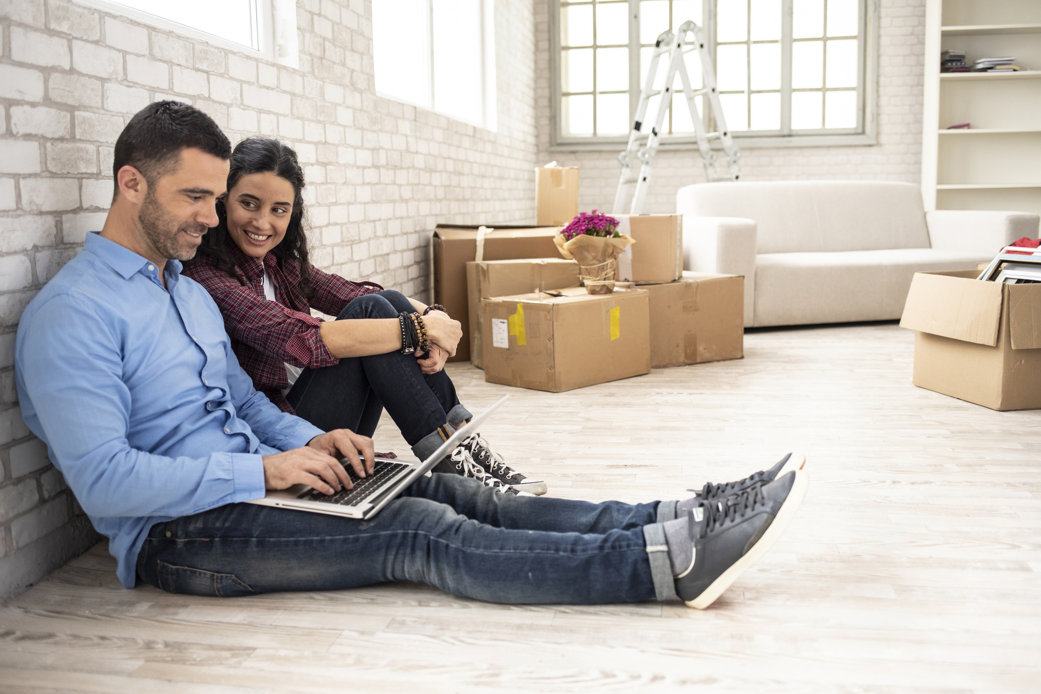 couple sitting on floor using a laptops with moving boxes in backround
