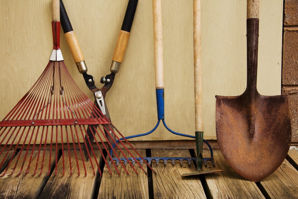 Outdoor lawn equipment including rakes and shovels propped against a wall in the garage.