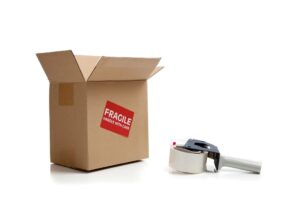 a moving box with a red fragile label on the side and a tape dispenser next to it.