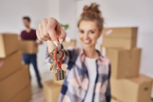 woman with moving boxes in the background handing over keys to a rental home.