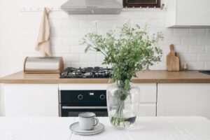 White kitchen with a cup and saucer staged next to a vase with water and fresh flowers.
