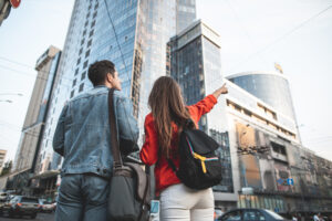 Delighted couple observing urban architecture together. man and woman are standing with their backs turned with backpacks. female is pointing with finger at skyscraper