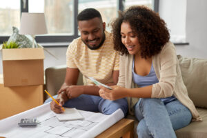 Couple planning a move with paper, pencil, and calculator and surrounded by moving boxes.