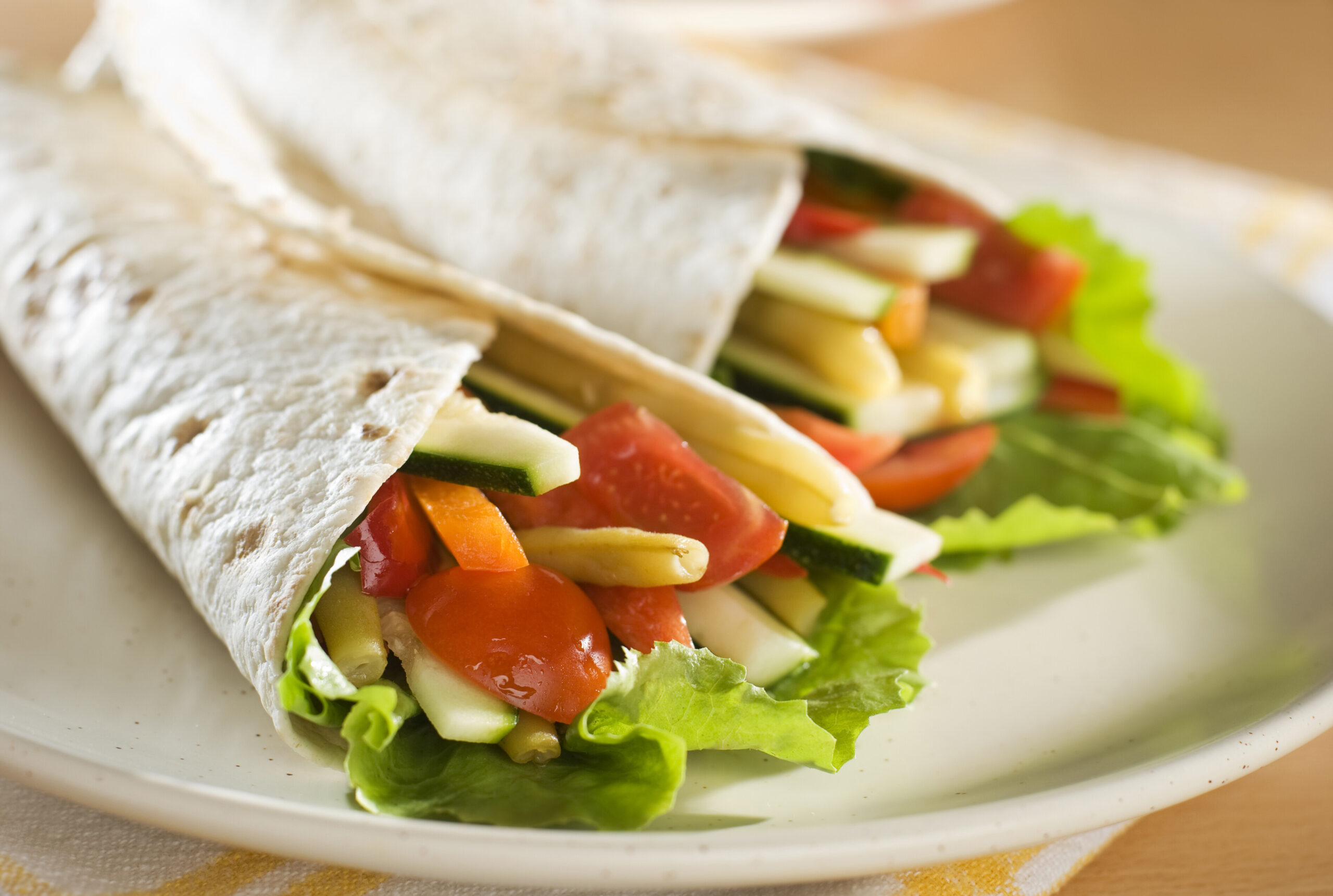 Two healthy veggie wraps on a white plate.