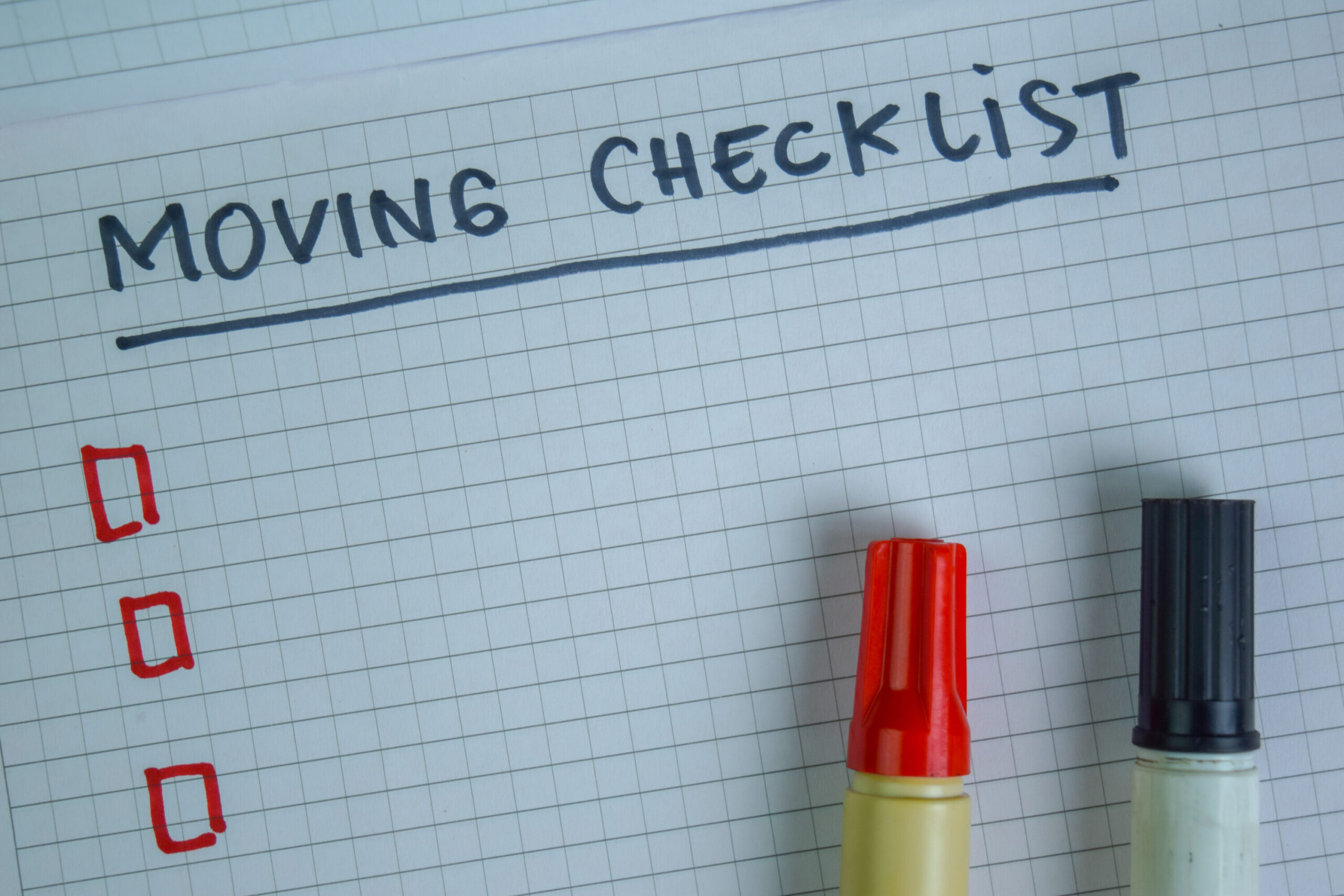 Graph paper with Moving Checklist written in marker and two markers resting on top.