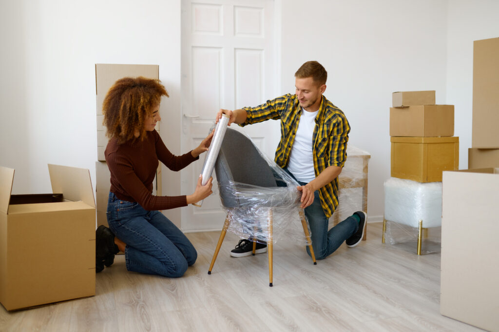 Woman and Man unwrap a modern chair with moving boxes in the background.