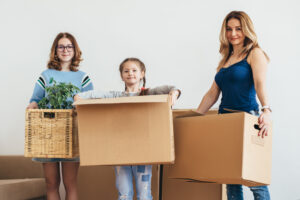 Mom with two young girls holding moving boxes in a rental home.