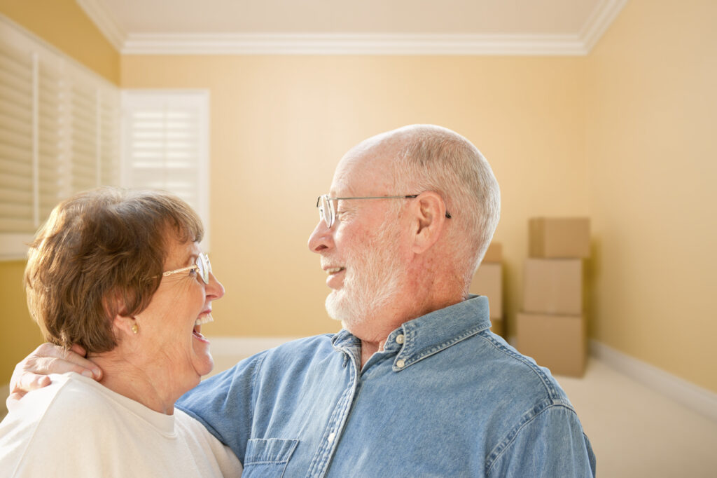 Happy senior woman and man in an embrace in front of moving boxes preparing to move.