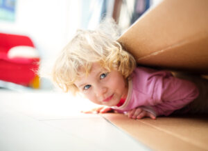 Child on laying on the floor under a moving box showing hesitation about moving.