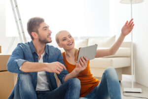 Man and woman sit on the floor with a tablet planning where furniture will be placed during a move.