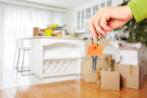 A hand holding out keys to a rental property with moving boxes in the background.